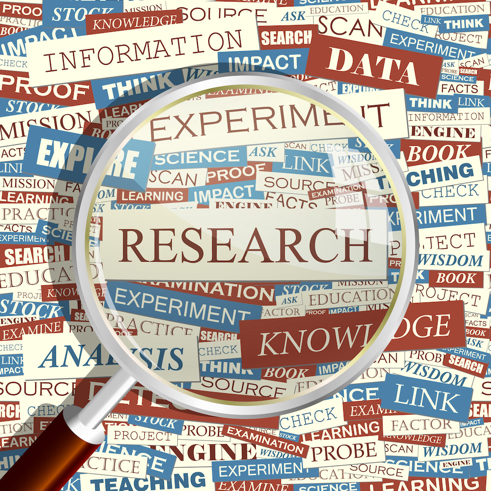 Magnifying glass highlighting the word “research” surrounded by other words. 