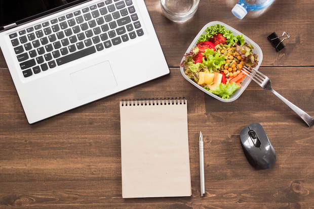  A computer, notepad, and healthy meal on a brown wooden desk. 