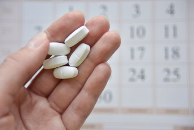 A hand holding pills in front of a calendar 