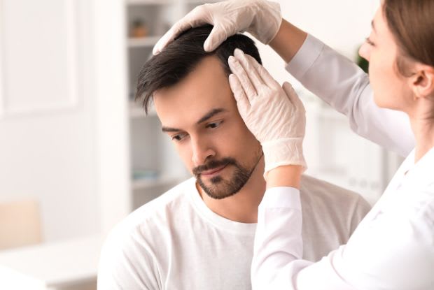 A doctor inspecting a man’s scalp for hair loss