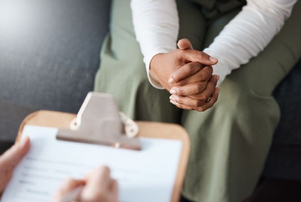 A woman with hands clasped talking to a doctor with a clipboard