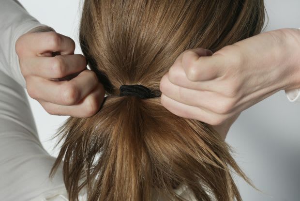 a woman tying her hair up in a ponytail