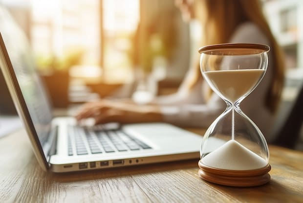 a woman on her laptop with an hourglass in the foreground