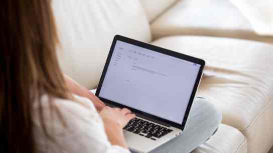Woman types email while sitting on her couch 