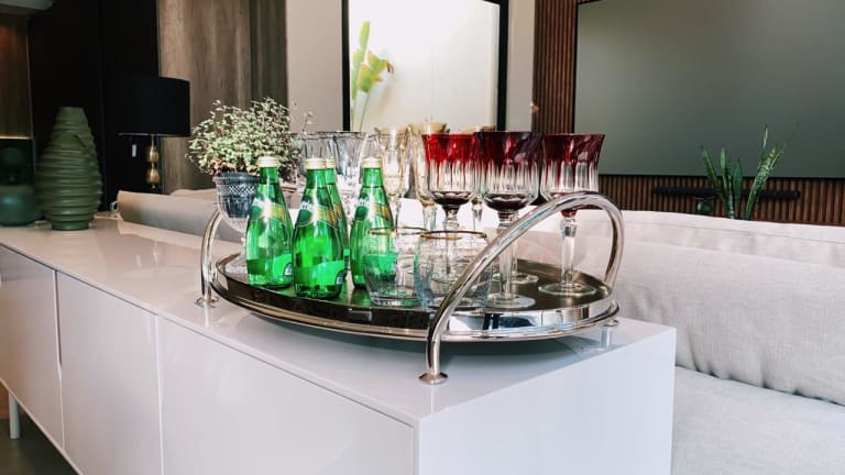 Bandeja grande de prata com alça, com taças coloridas e garrafinhas de água.