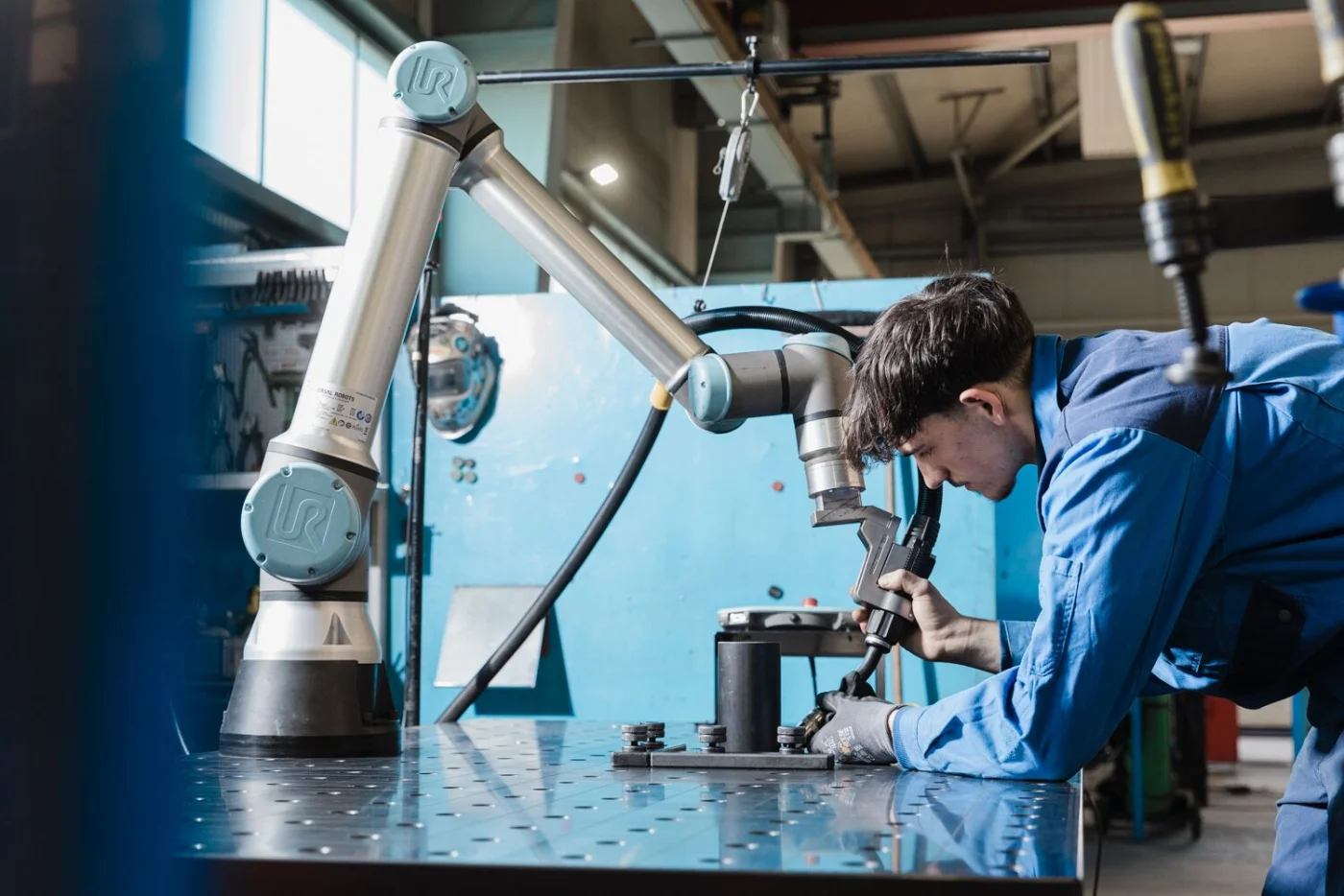 A worker collaborates with a Universal Robots collaborative robots arm at an assembly workbench, no safety cage required
