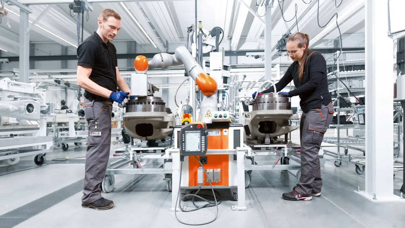 A KUKA lightweight collaborative robot performing precision tasks alongside a human worker on a fenceless factory floor under ISO/TS 15066 human-robot collaboration standards