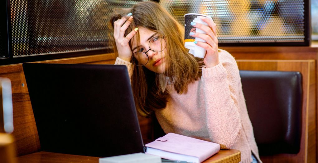 A woman sitting at a table with her laptop and a cup of coffee, frustrated with a complex booking system.