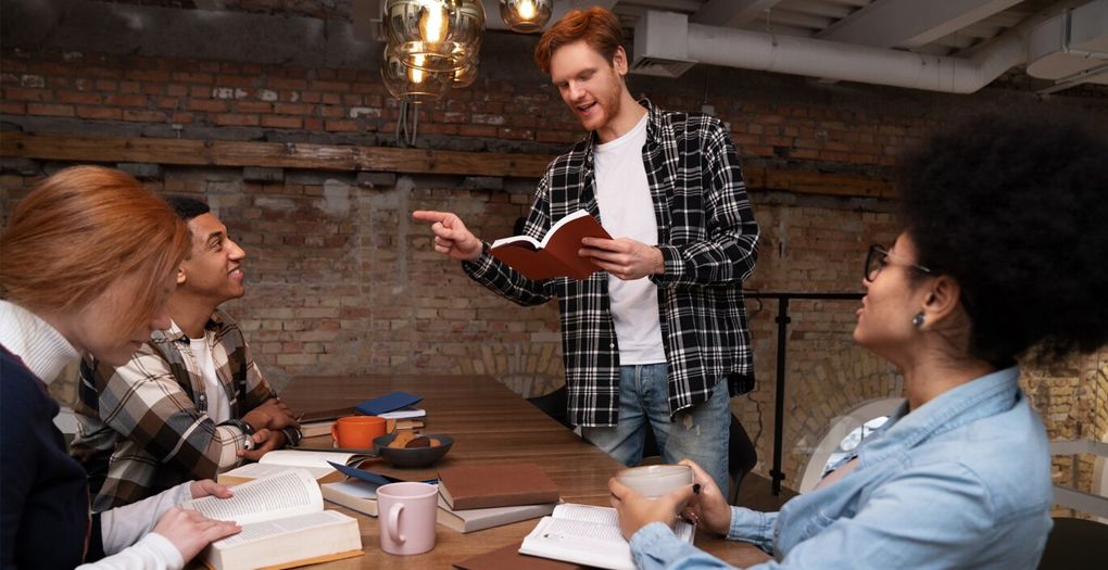 A person is explaining something from a book to three of his colleagues.