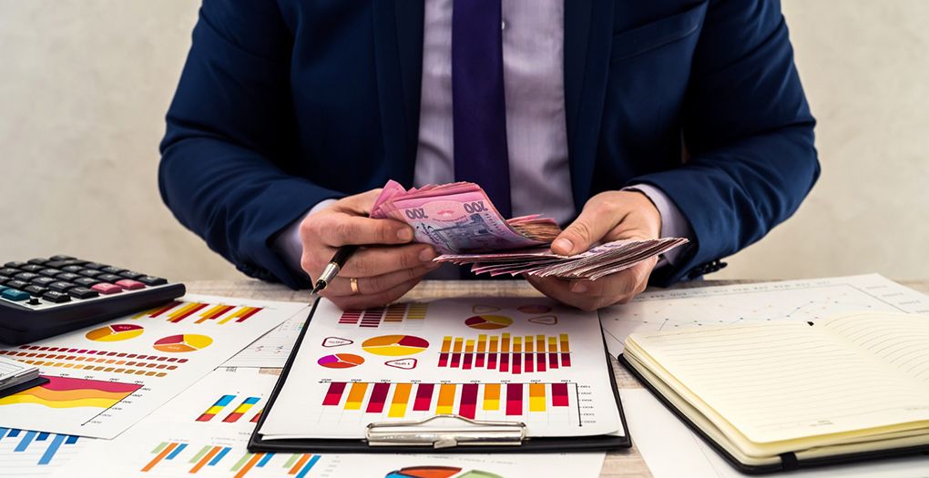 A businessman counting money on a desk with a calculator and papers.