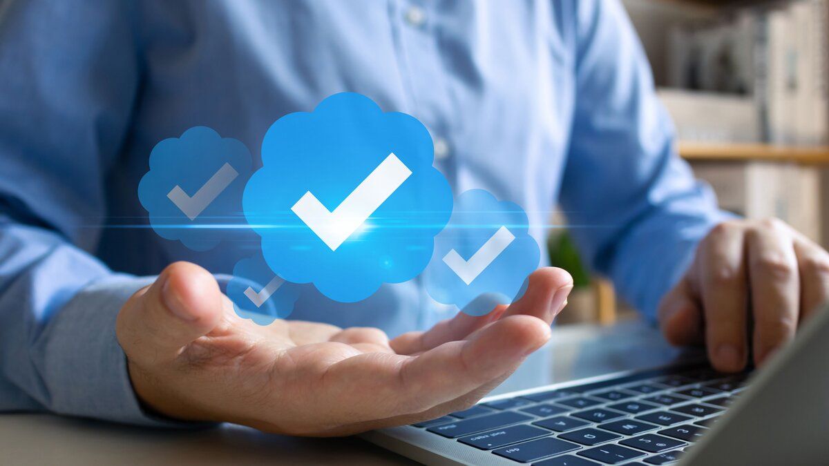 A man at a computer with three checkmark floating in his hand to depict social verification