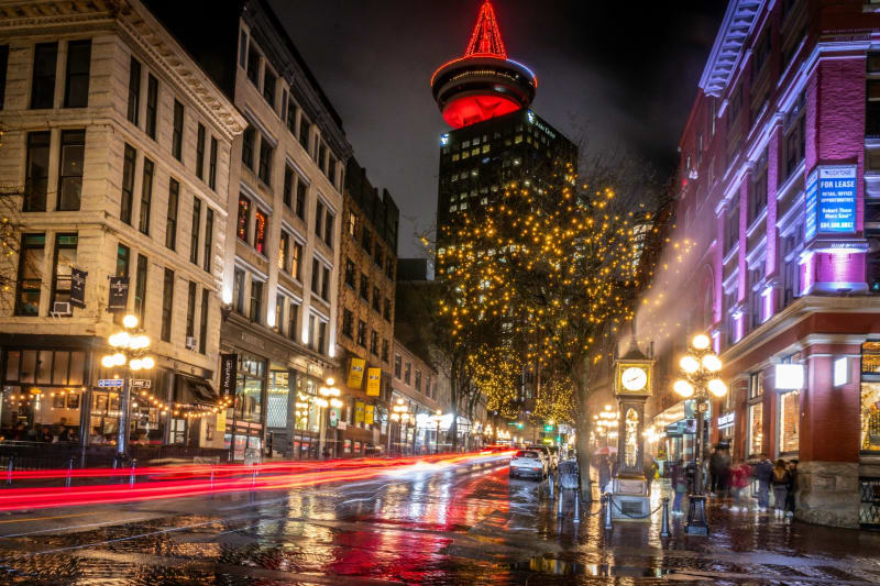 A time lapse photo of traffic by the Gastown steam clock with the Harbour Centre in the background.