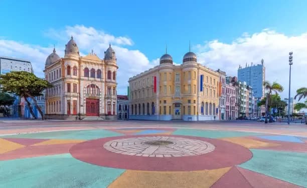 Praça com grande mosaico circular colorido no piso e casarões históricos amarelos ao fundo.