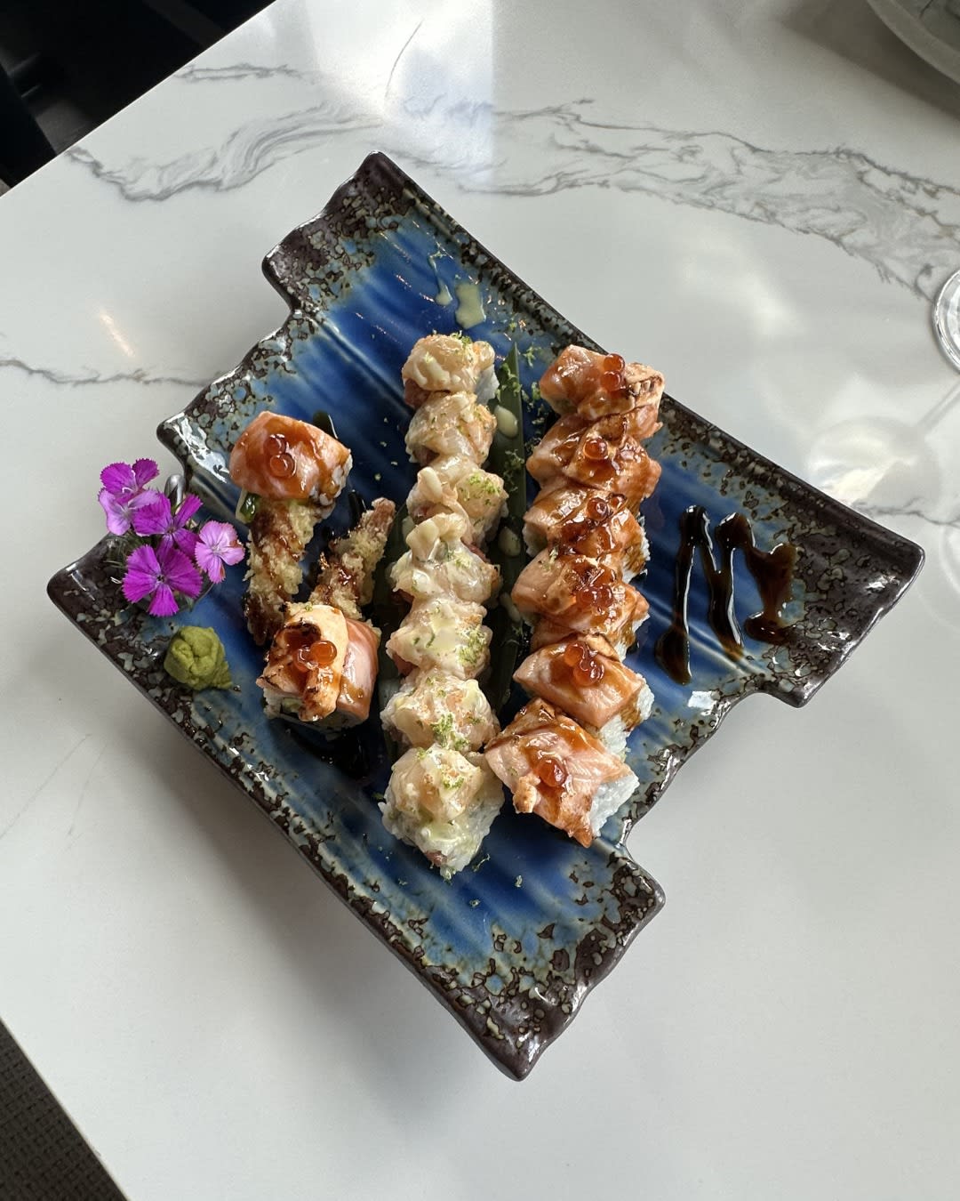 Multi-roll platter on blue triangular ceramic at Izumi Sushi Castle Rock — Izumi Roll center flanked by Toro Uni Rolls