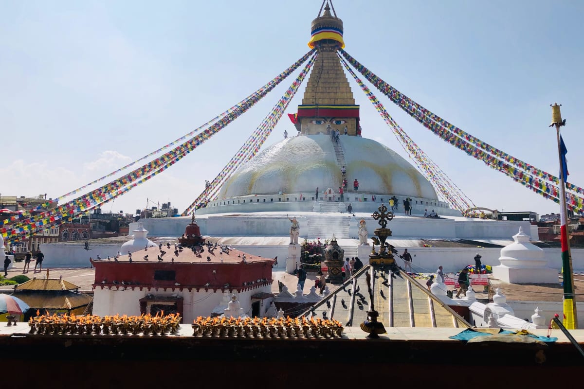 The white dome and gilded tower of Boudhanath Stupa in Kathmandu under a blue sky, hung with prayer flags