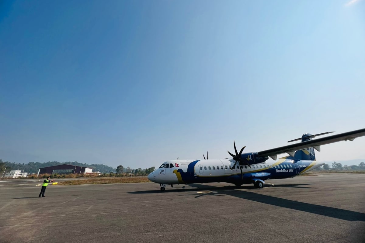 A twin-propeller passenger plane parked on an airport apron under a clear blue sky in Nepal