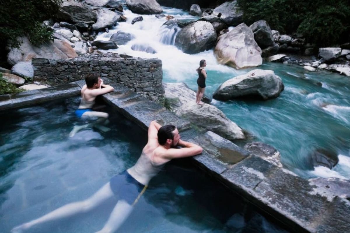 Trekkers relaxing in the stone-lined natural hot spring pools beside the river at Jhinu Danda