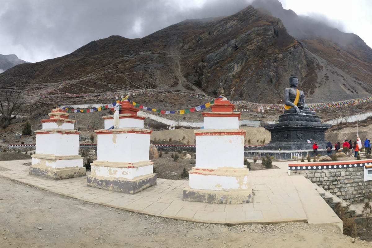 A row of red and white chortens on a dry hillside in Upper Mustang with snow peaks behind