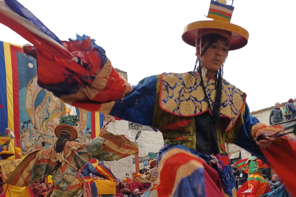 A masked monk dancer in a brocade costume and wide hat performing at the Tiji festival in Lo Manthang