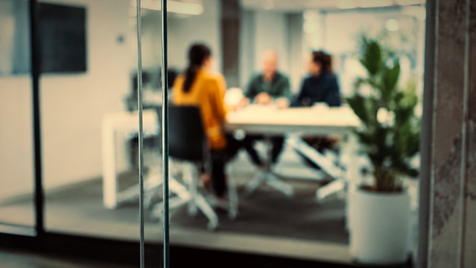 A meeting in progress inside a glass-walled conference room, seen from the corridor outside.