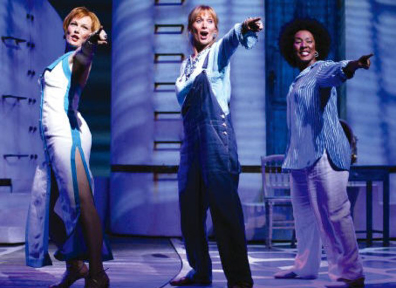 Three middle aged women siging and striking a pose by pointing into the audience