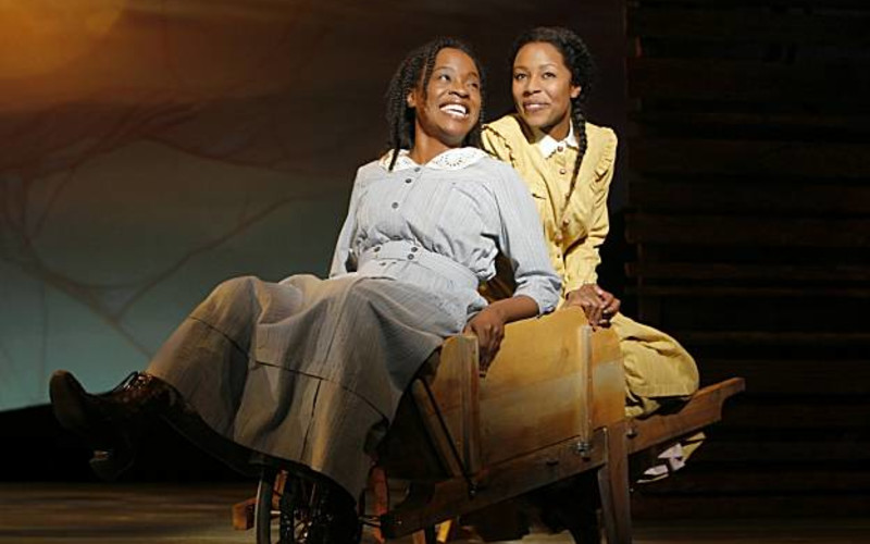 Two sisters sit in a wheel barrel smiling with each other