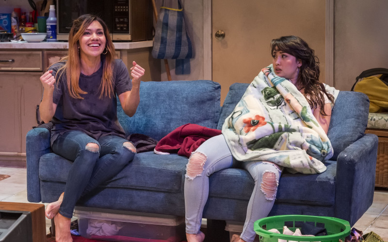 A mother and her high school daughter sit on their living room sofa in conversation.