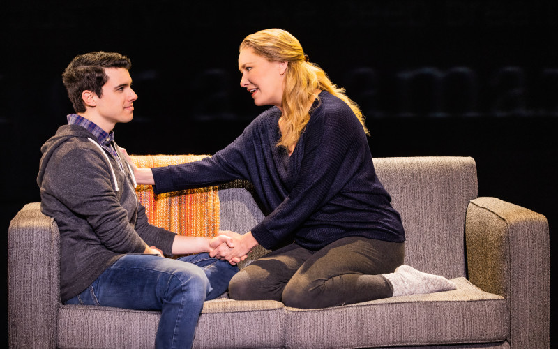 A mother and her high schools son sit on their living room sofa in conversation.