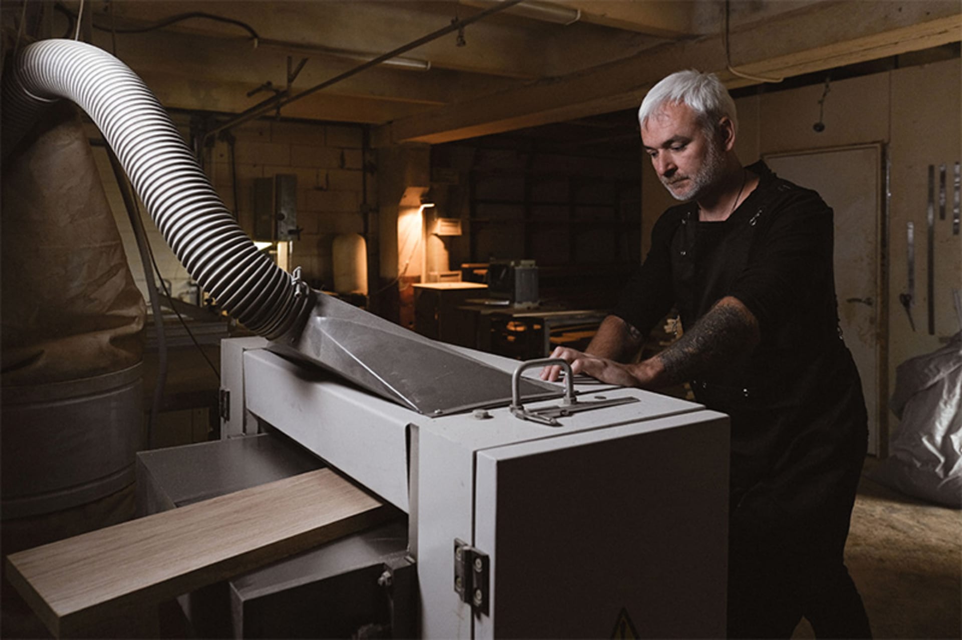 Worker operating a stationary wood sanding machine with a dust extraction hose and a board on the feed table