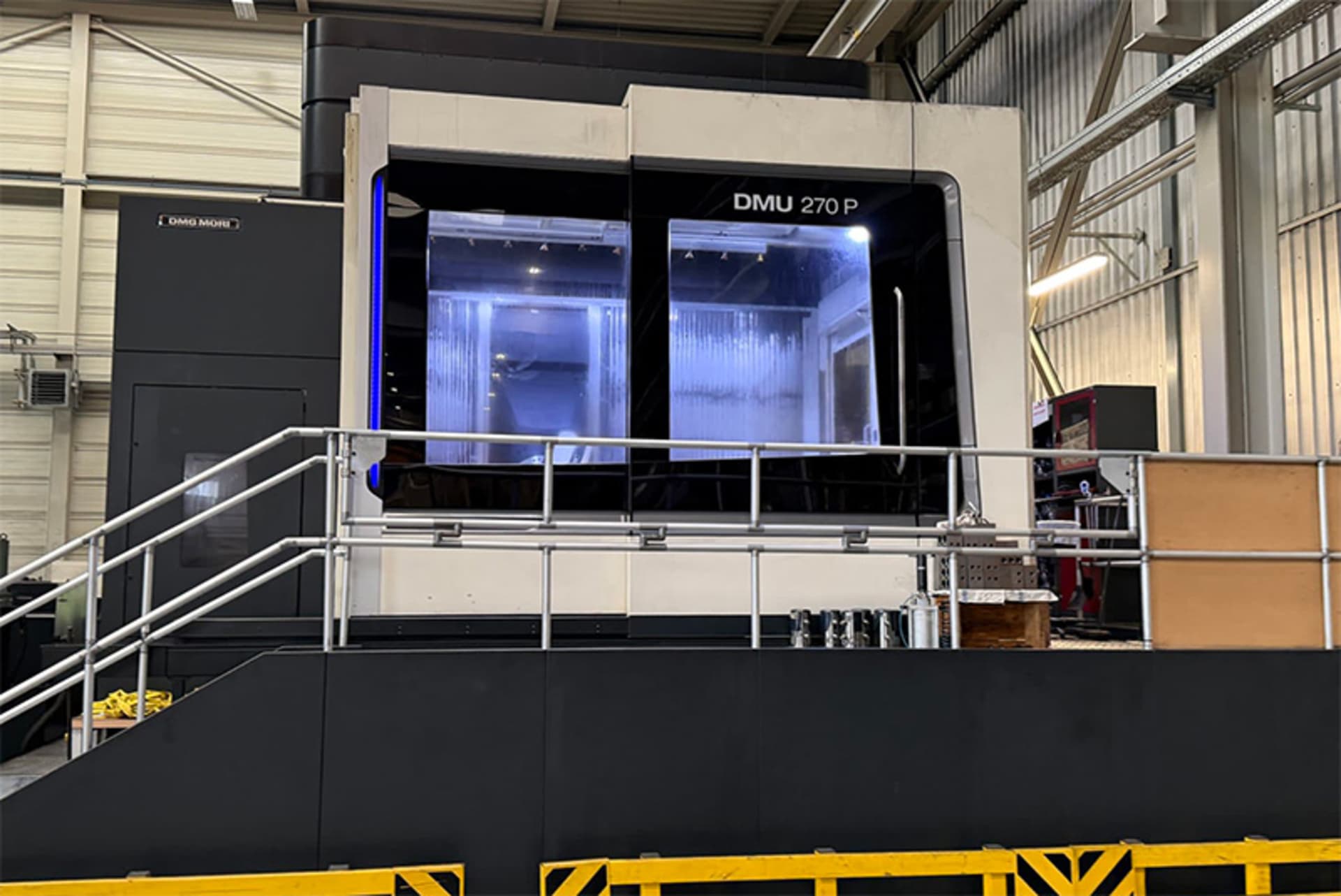 Front view of the DMG MORI DMU 270 P with an illuminated working area and a raised operator platform with safety railings