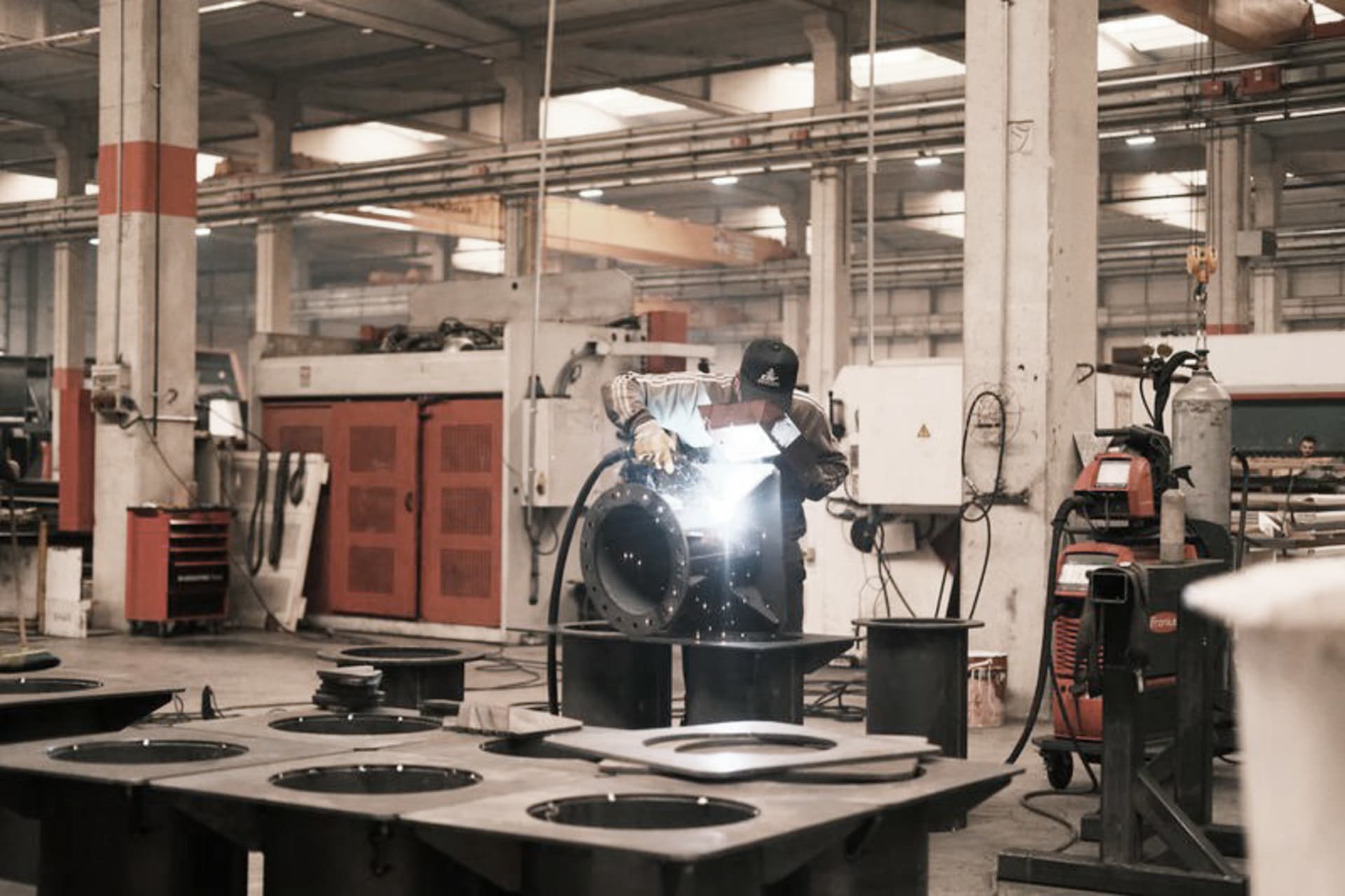 Schweißer mit Schutzhelm beim Schweißen eines großen Metallbauteils in einer Industriehalle