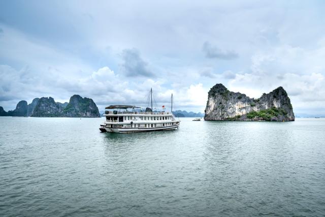 Thuyền gần đảo đá vôi và mặt nước xanh — cảm giác dừng đảo / điểm bơi trên vịnh Hạ Long
