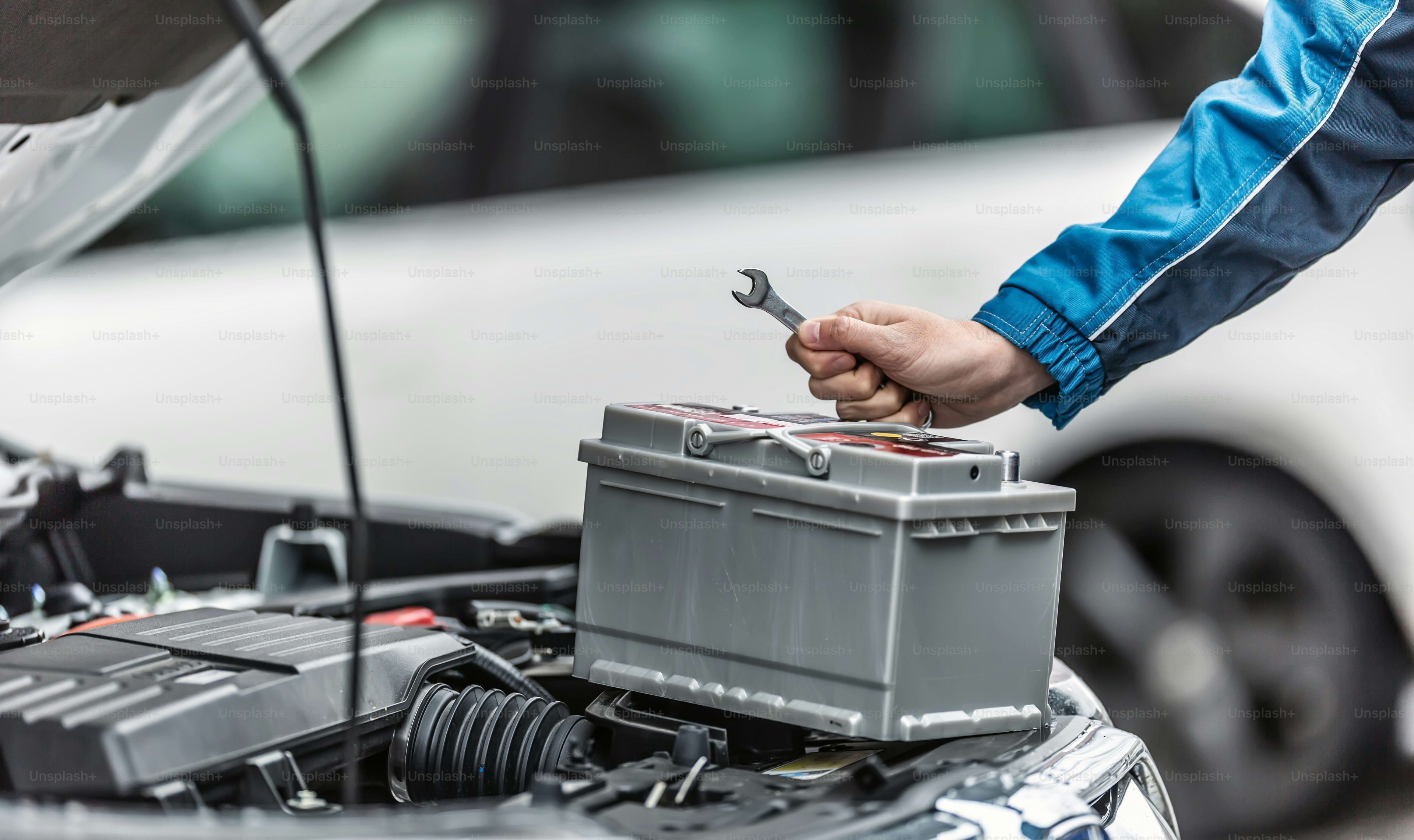 Mechanic with a wrench next to a fresh car battery in the engine bay