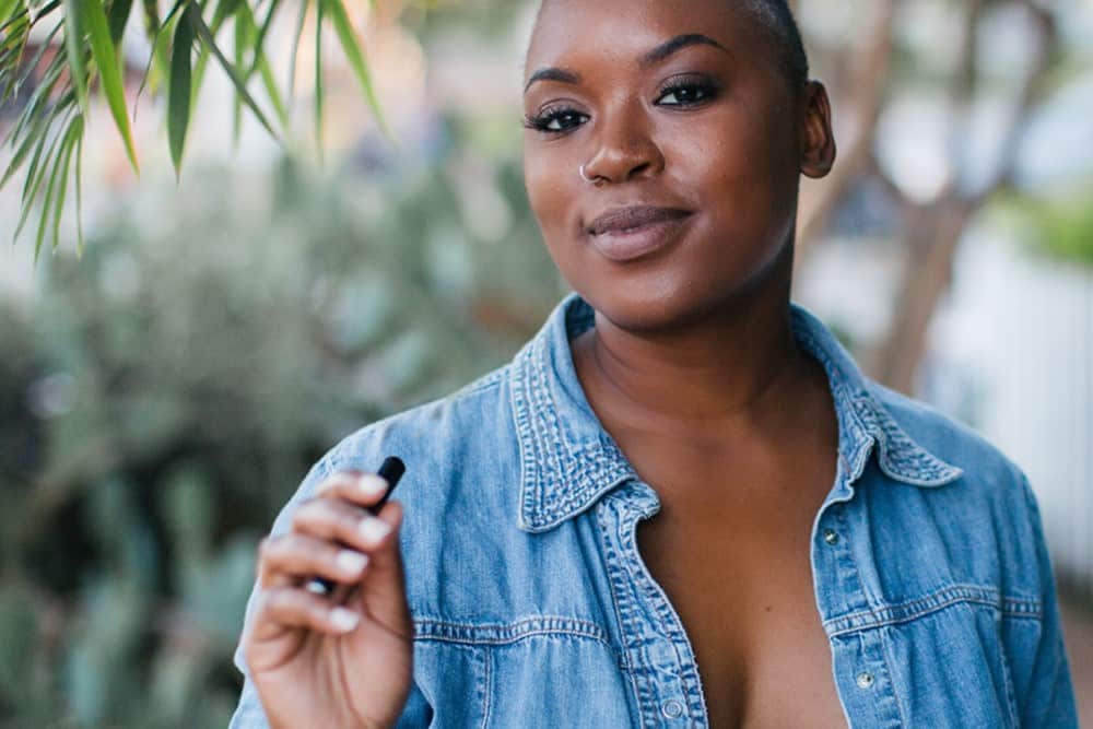 A woman wearing a blue shirt holds a black vape pen