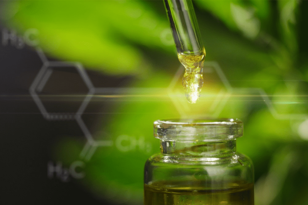 A golden dropper of full spectrum CBD rests on a green, leafy background