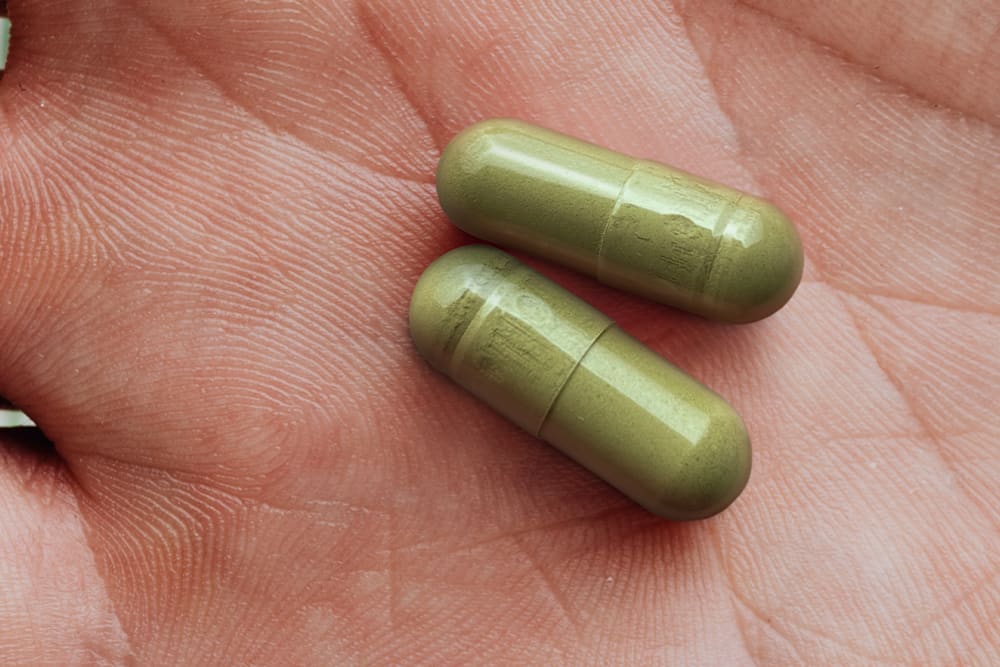 Two kratom capsules in the palm of a hand