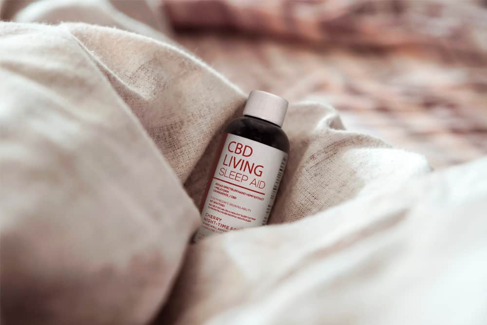 A bottle of CBD Living CBD syrup sits in a fluffly blanket