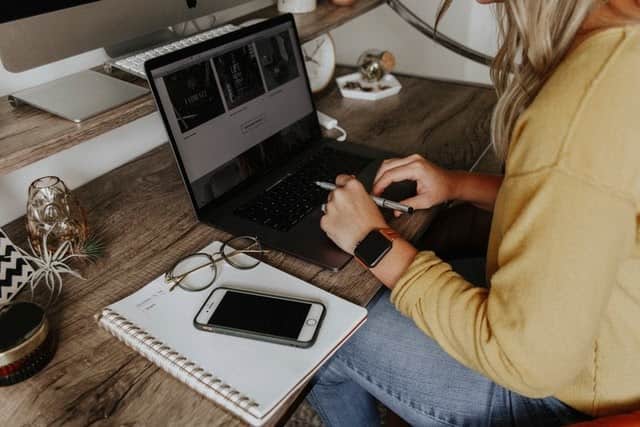 A woman working on a laptop at a desk with a notebook.