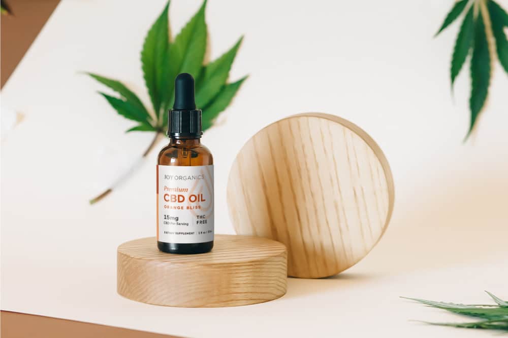 A tincture of CBD oil atop a round wooden discus, hemp leaf aloft to the left