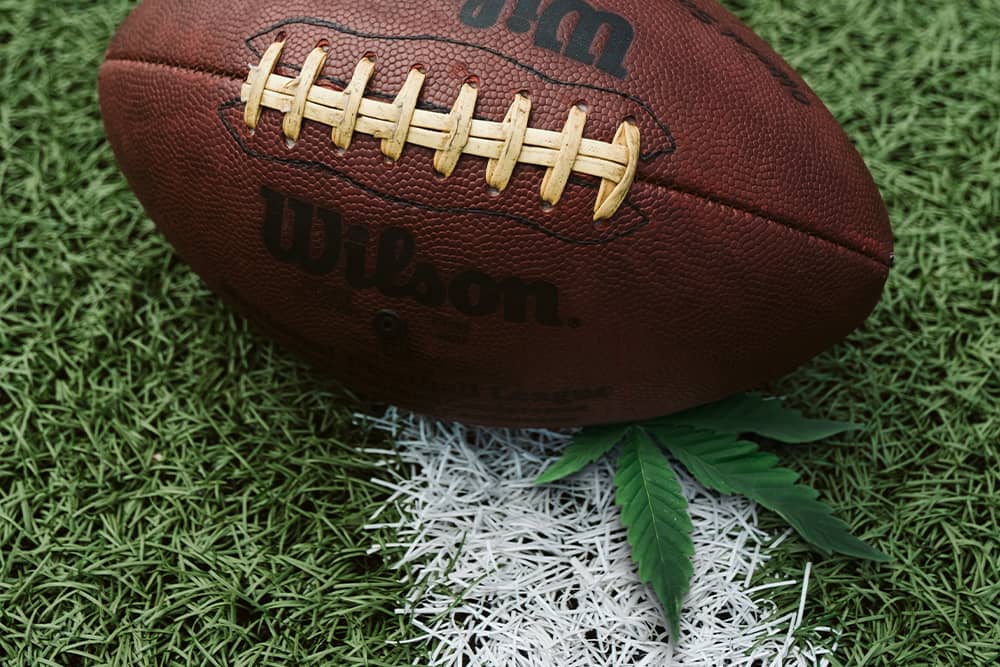 A cannabis leaf beneath an NFL football on a turf football field.
