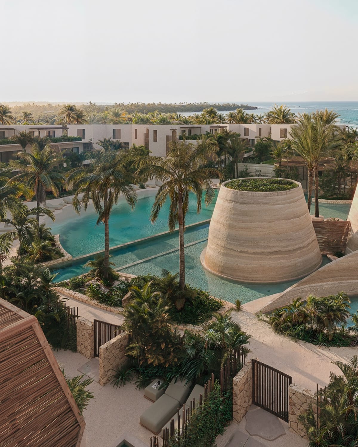 Lagoon pools and woven pavilions among the low buildings, the sea beyond, Samaná Loft Villa · Render