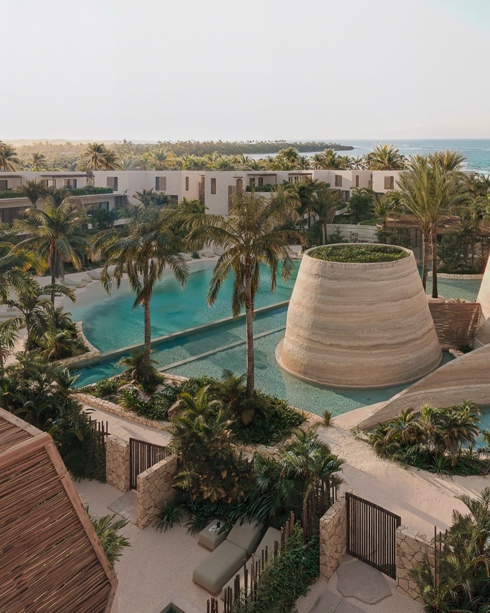 Lagoon pools and woven pavilions among the low buildings, the sea beyond