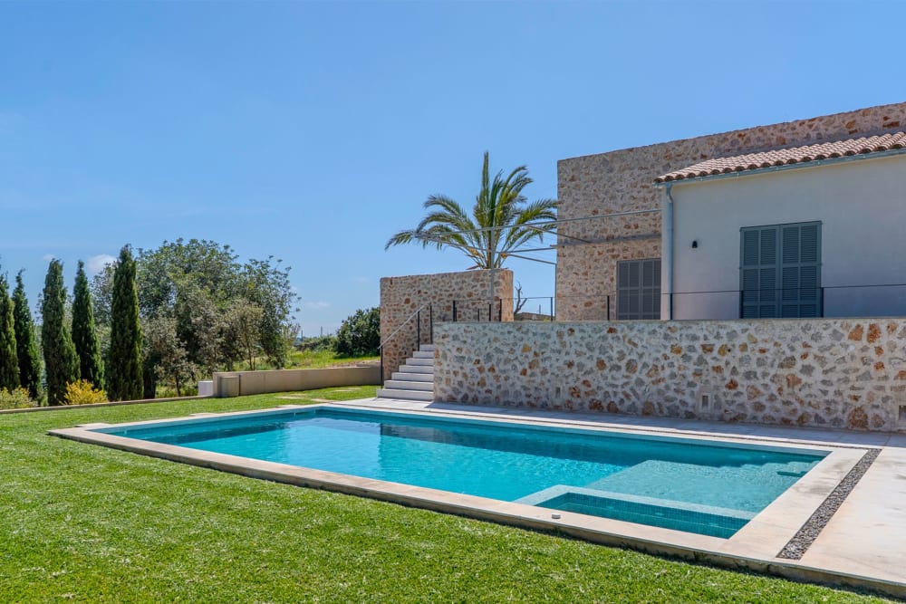 Der Pool entlang der steinernen Terrassenmauer, dahinter Zypressen und Olivenbäume, Finca Sant Llorenç