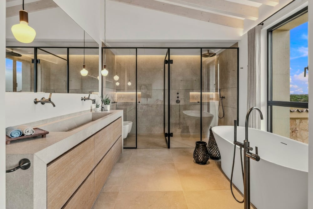 Ein Badezimmer mit freistehender Badewanne, langem Waschtisch aus Eiche und einer Dusche mit Glaswand, Santanyí III