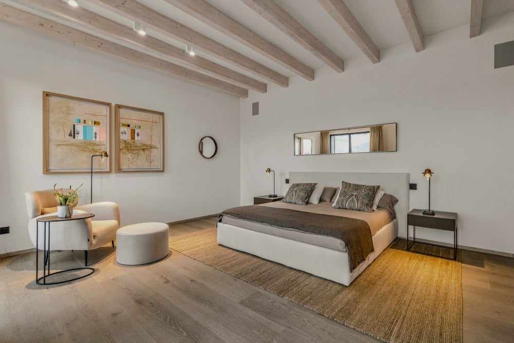 Ein Schlafzimmer mit einem beigen Bett, zwei Sesseln und Balkendecke, Santanyí III