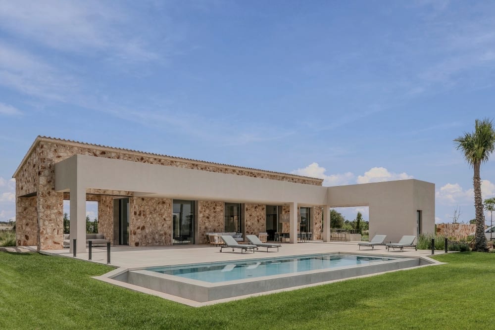 Der lange rechteckige Pool auf dem Rasen, vor einem eingeschossigen Steinflügel und einer überdachten Terrasse, Santanyí III