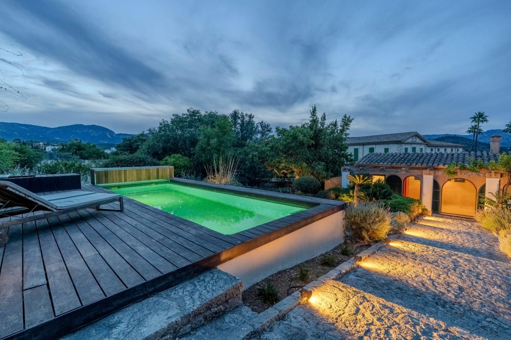 Der beleuchtete Pool in der Dämmerung, dahinter die Berge, Exklusive Gartenwohnung