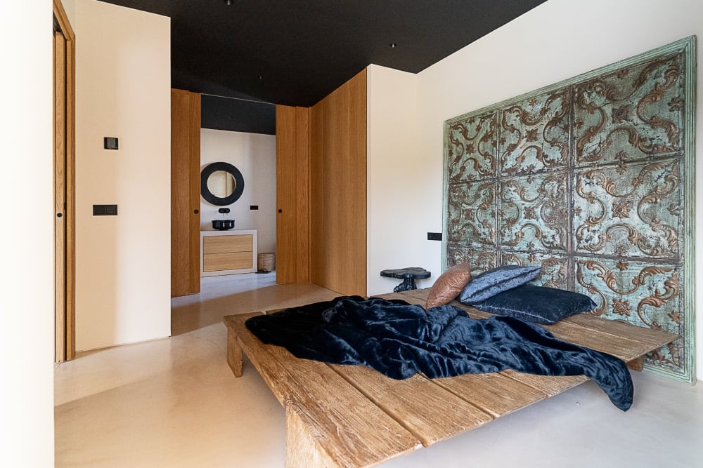 Bedroom with a low wooden bed and a carved panel behind it, Falco 10