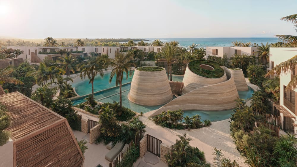 Lagoon pools and woven pavilions among the low buildings, the sea beyond, Samaná Loft Villa · Render