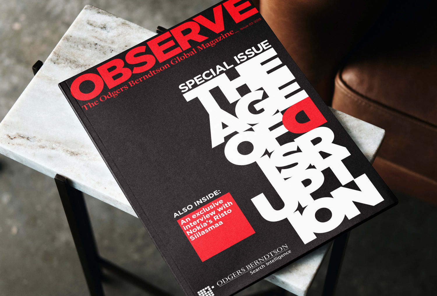 The Observe magazine showing the cover. The magazine is laid on a small table with a white marble top. The photo also includes a section of a leather sofa in the background.